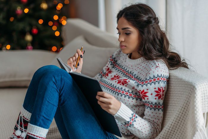 Understanding-How-the-Holiday-Season-Can-Affect-Your-Sobriety - woman in holiday sweater journaling