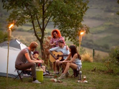 group of young friends camping at dusk, drinking and playing guitar - turn down alcohol