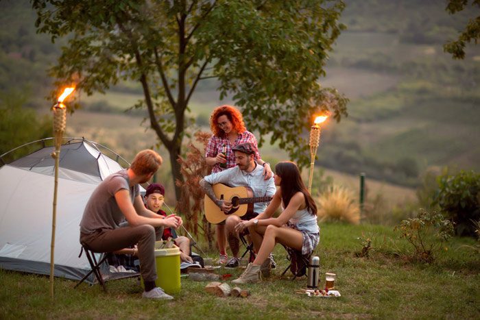 group of young friends camping at dusk, drinking and playing guitar - turn down alcohol