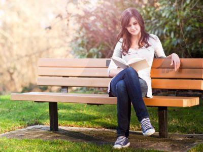 young brunette woman on park bench reading a book - depression and anxiety