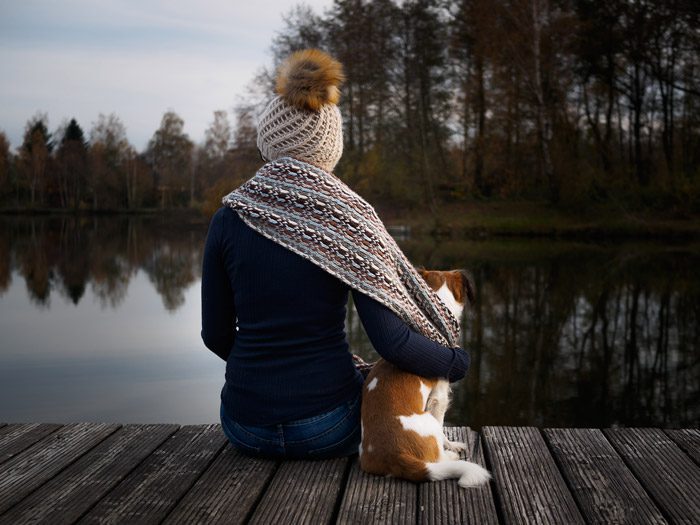 woman sitting on dock with her arm around her dog, facing away from the camera - mindfulness