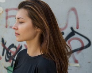 pretty brunette woman with eyes closed standing against concrete wall with graffiti on it - urge surfing