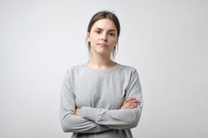 young woman with arms crossed on gray background - excuses