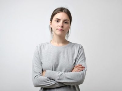 young woman with arms crossed on gray background - excuses