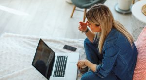 young woman sitting on bed with laptop using video conferencing - telehealth
