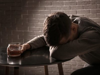 depressed man sitting at table in dark room holding glass of liquor - depression