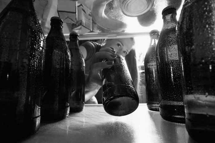 black and white image of woman reaching for a beer in refrigerator full of beer bottles - blackouts