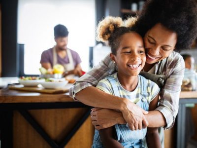 beautiful Black family - smiling mom hugging young daughter from behind in the kitchen