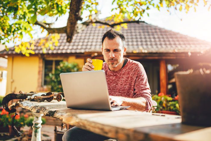 man working on laptop in backyard on sunny day - spending time in nature