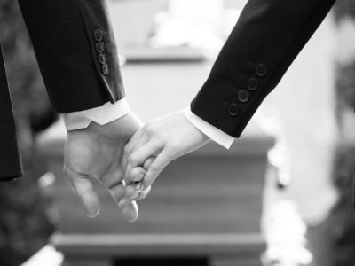 black and white image of two people holding hands in front of a casket - overdose