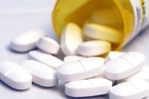 prescription pill bottle laying on its side with white oval tablets spilling out - Vicodin addiction