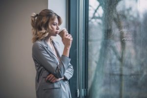 pretty young businesswoman looking out window drinking coffee - willpower and recovery
