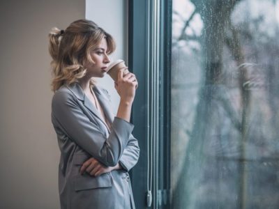 pretty young businesswoman looking out window drinking coffee - willpower and recovery