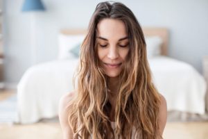 pretty young woman with long hair sitting on the floor of her room with her eyes closed - grounding techniques