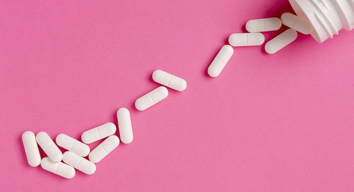 bottle of white pills spilling onto pink background - tramadol addiction