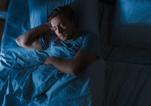 Sleep Hygiene in Recovery, dark cool toned image from above of man sleeping in his bed - sleep hygiene