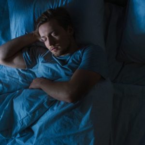 Sleep Hygiene in Recovery, dark cool toned image from above of man sleeping in his bed - sleep hygiene