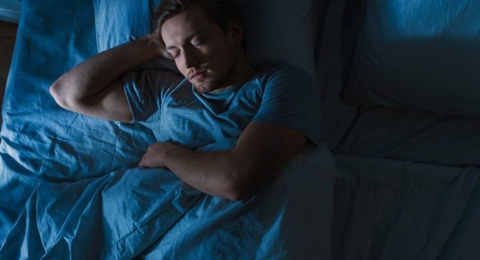 dark cool toned image from above of man sleeping in his bed - sleep hygiene