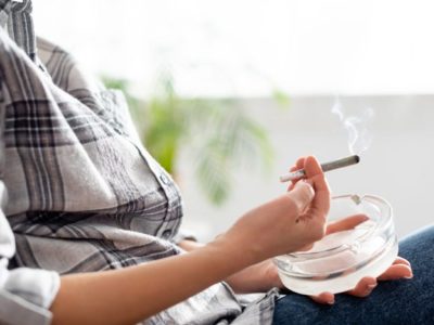 cropped shot from neck down of older woman in a plaid shirt smoking a marijuana cigarette