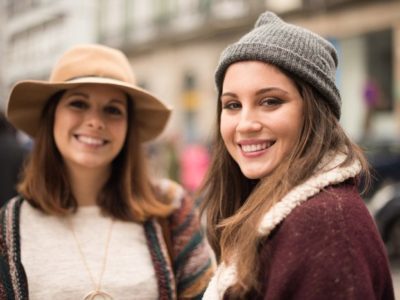 two pretty and stylish young women walking outside together, stopped and smiling at the camera - codependency