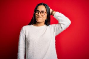 Signs You Might Be a Functional Alcoholic, young woman scratching the back of her head as if she is thinking - against a red background - functional alcoholic