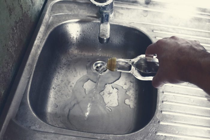 cropped shot of a man's hand pouring liquor down the sink drain - alcohol withdrawal