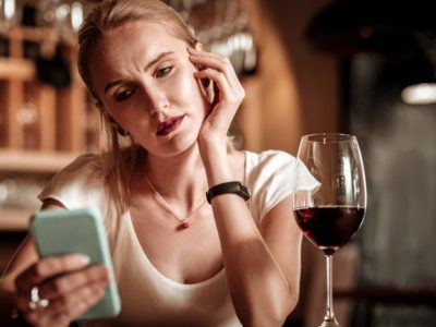 pretty blonde woman having a glass of red wine and looking at her cell phone - gray area drinking