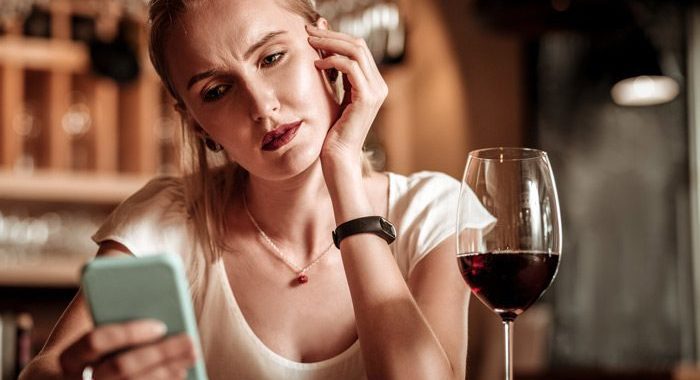 pretty blonde woman having a glass of red wine and looking at her cell phone - gray area drinking