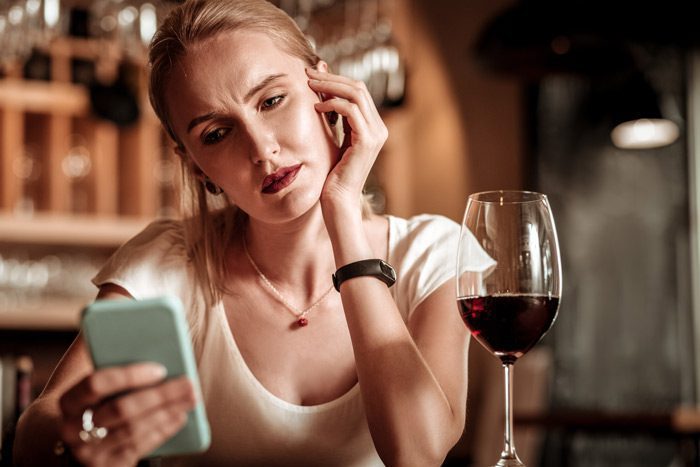 pretty blonde woman having a glass of red wine and looking at her cell phone - gray area drinking