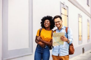 beautiful, young multi-racial couple smiling and looking at map as they walk down a street - sober vacation