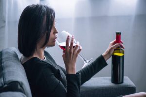 depressed lonely woman sitting on couch and drinking wine at home