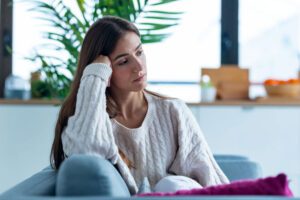 Photo of a woman who looks unhappy sitting on her couch in contemplation