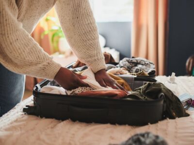 Person organizing clothes and personal items into an open suitcase on a bed in a softly lit room.