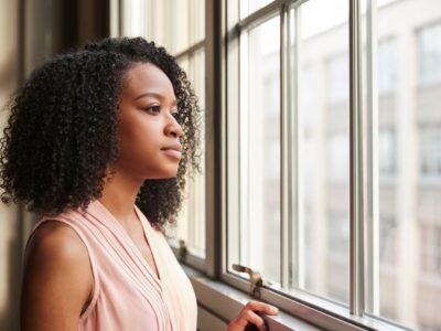 A thoughtful young woman stands by a window, gazing outside with a calm, reflective expression, symbolizing resilience and managing cravings in recovery.