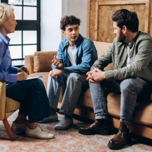 Family therapy session with a teenager talking while sitting between two adults, symbolizing open communication and support in recovery.