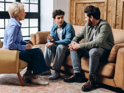 Family therapy session with a teenager talking while sitting between two adults, symbolizing open communication and support in recovery.