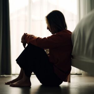 Waypoint Recovery - What’s Contingency Management for Meth Dependence. A shadowed woman sits in a poorly lit bedroom on the floor at the end of her bed. The woman appears to be upset.