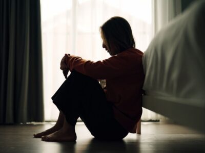 Waypoint Recovery - What’s Contingency Management for Meth Dependence. A shadowed woman sits in a poorly lit bedroom on the floor at the end of her bed. The woman appears to be upset.