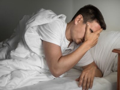 A person sitting on a bed with their head in their hand, appearing distressed. The image depicts a man struggling with StUD.