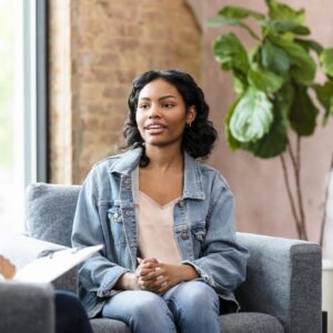 Waypoint - What’s Psilocybin-Assisted Psychotherapy For SUD. A young womans sits in a therapy session speaking with a therapist taking notes on a clipboard.