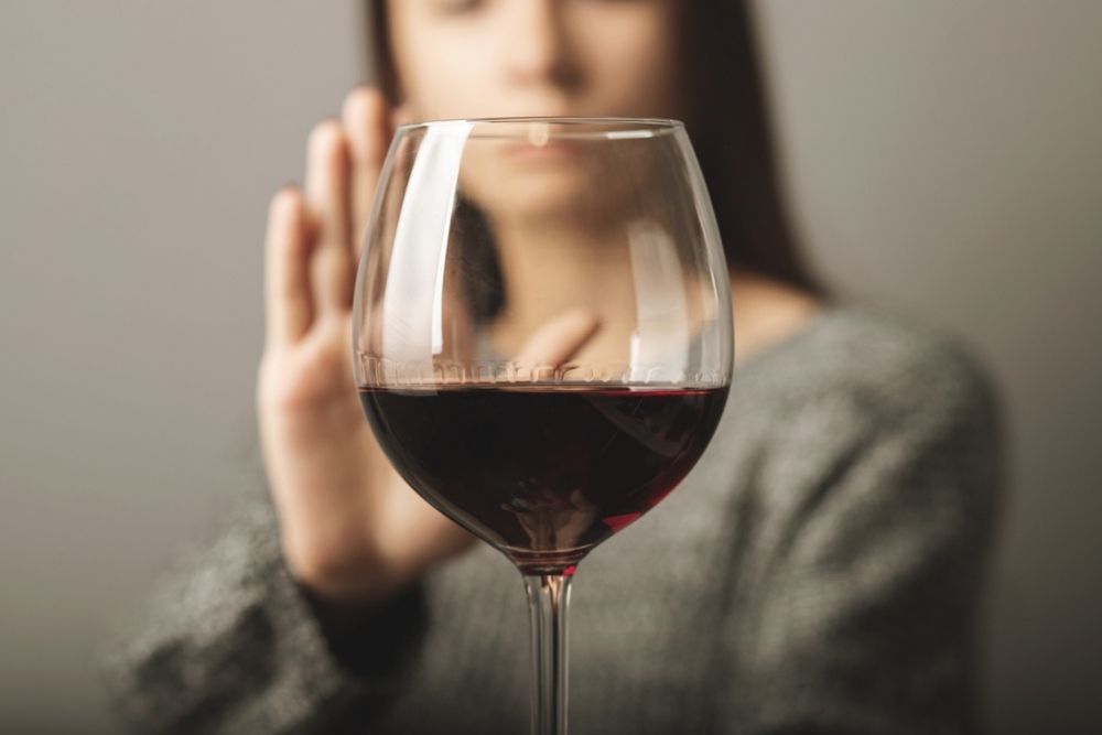 A woman holds up her hand in a gesture of refusal behind a large glass of red wine, signaling that she does not want to drink.