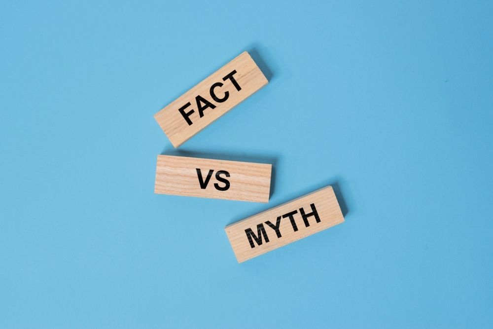 Three wooden blocks on a blue background display the words FACT, VS, and MYTH, with VS positioned between the other two blocks.