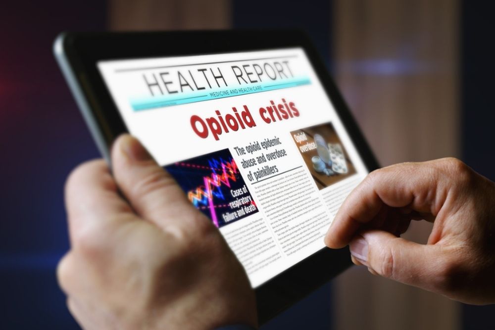 Person holding a tablet displaying a health report with the headline Opioid crisis in bold red letters, accompanied by text and images related to the opioid epidemic.