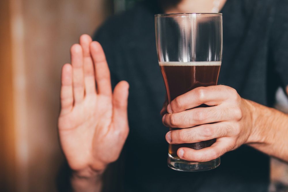 A person holding a glass of dark beer while making a hand gesture to decline it.